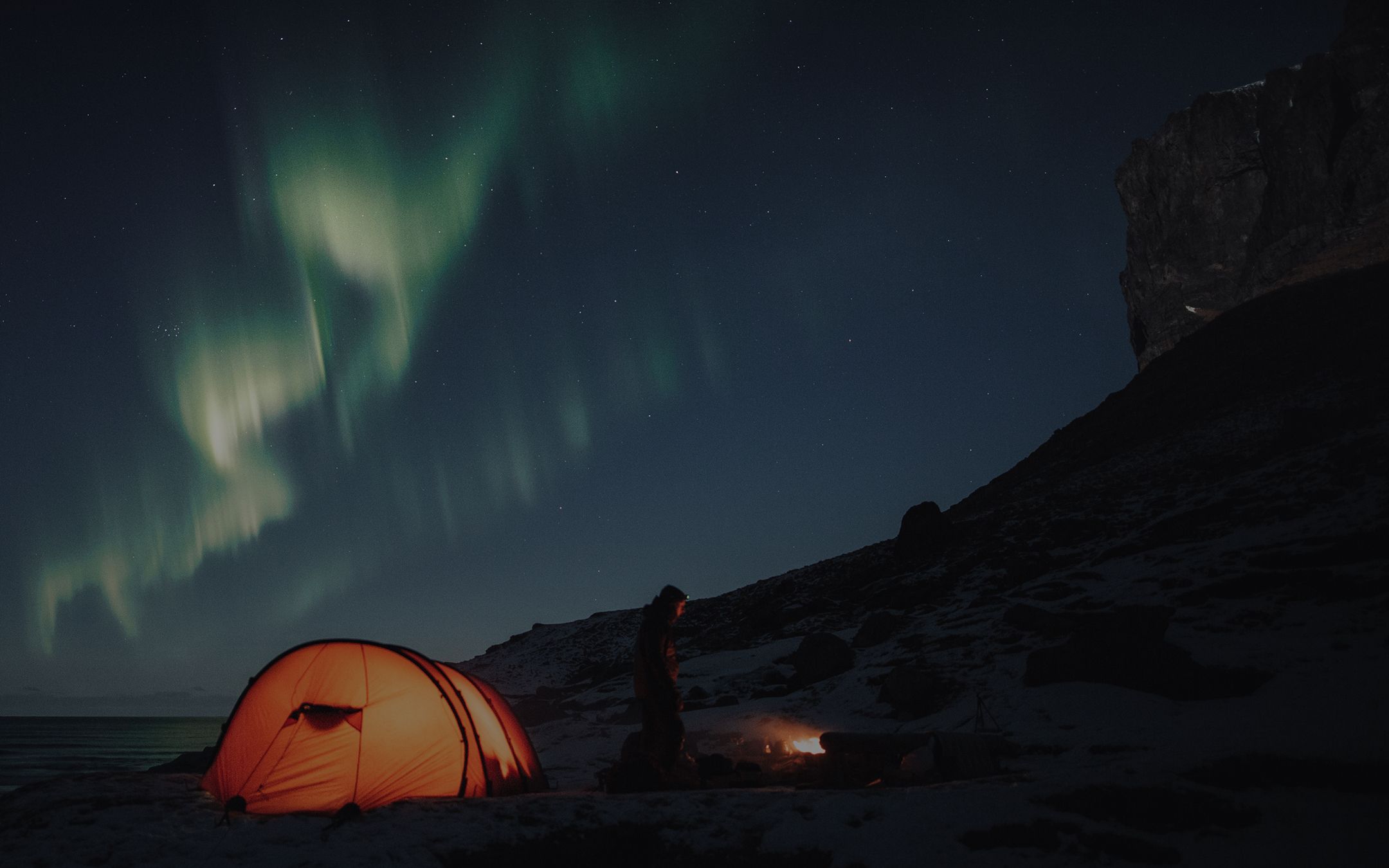 Northern lights above mountains with tent and couple symbolizing financial guidance and discovery