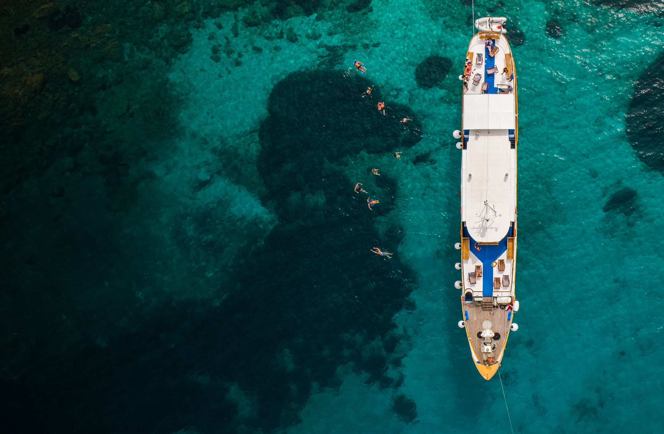 Yacht anchored in clear ocean water with swimmers